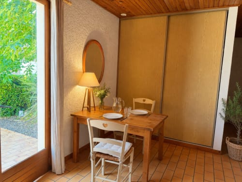 Coin repas du studio à Côte Landes, Mimizan avec table en bois, miroir, lampe et accès à la vue sur le jardin