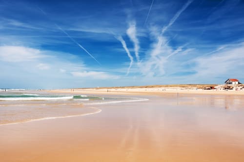 Plage de sable idyllique à Mimizan avec vagues turquoise, maison côtière au toit rouge et ciel bleu dégagé