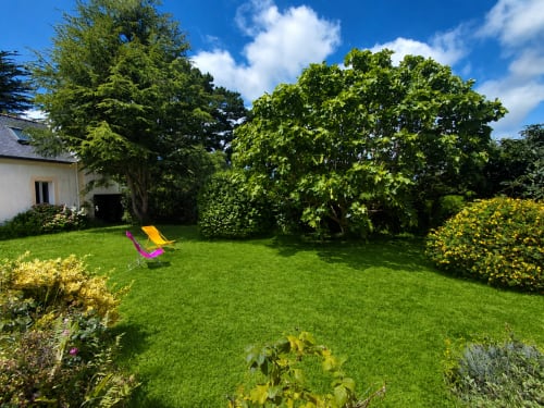 Jardin ensoleillé du gîte Maison Lannivrec à Locmaria, Belle-Île-en-Mer, avec pelouse verte, chaise longue colorée et fleurs