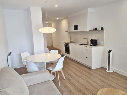 Moderno apartamento diáfano en Sanxenxo Silgar con mesa de comedor, cocina blanca, suelos de madera e iluminación colgante