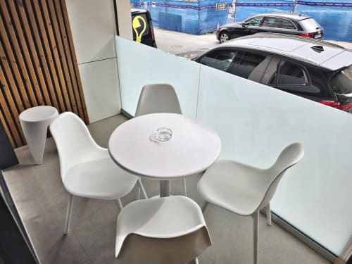 Moderna zona de descanso en BR SILGAR Sanxenxo con mesa redonda blanca, sillas y vista de vehículos estacionados en la sala de exposición