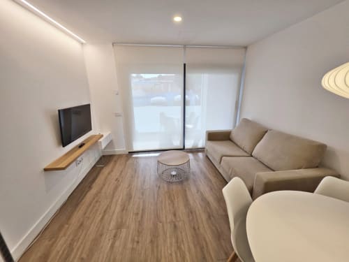Sala de estar moderna en Sanxenxo con sofá beis, televisor, suelo de madera y puertas de vidrio hacia balcón