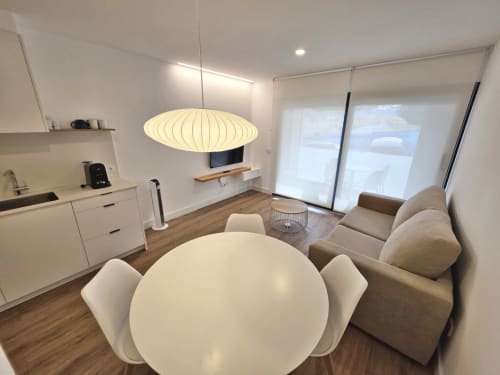 Moderno espacio de estar en BR Silgar Sanxenxo con mesa de comedor, sofá, cocineta, lámpara colgante y acceso a terraza