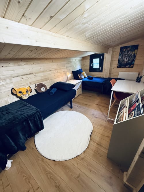 Chambre cosy du lodge en bois avec lits jumeaux, literie bleue, tapis blanc rond, bureau et décor de montagne