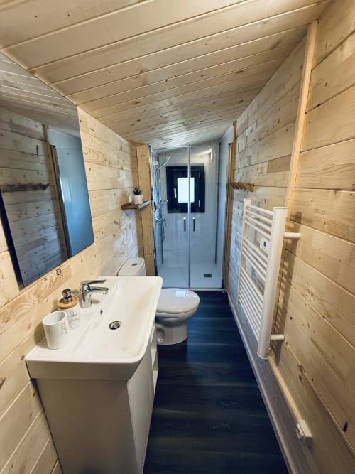 Salle de bain élégante du lodge en bois avec lavabo blanc, toilettes et douche à l'italienne aux Cabanes et lodges du Belvédère