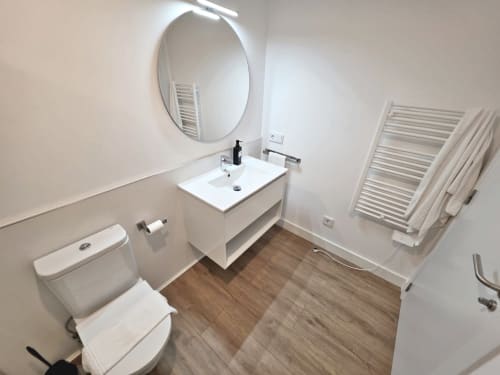 Baño moderno en apartamento BR SILGAR Sanxenxo con lavamanos blanco, inodoro, toallero climatizado y espejo redondo