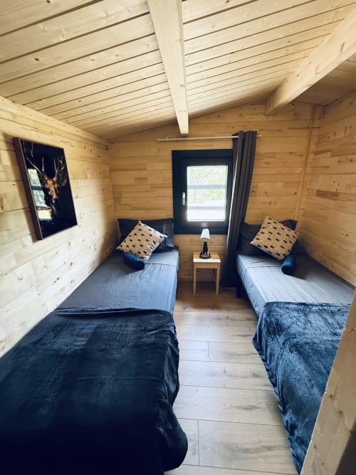 Chambre twin accueillante dans un lodge rustique en pin avec literie bleue, plafonds en bois et vue sur la montagne