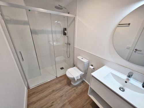 Baño moderno en BR SILGAR Sanxenxo con ducha de cristal, lavabo blanco, inodoro y suelos con efecto madera