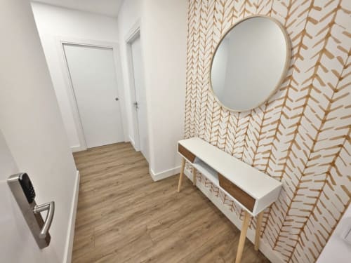 Recibidor moderno del apartamento BR SILGAR Sanxenxo con papel pintado geométrico, espejo redondo, consola y piso de madera