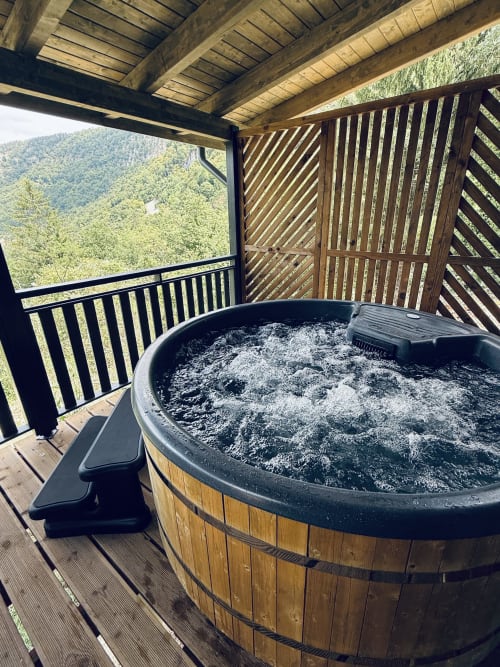 Bain à remous bouillonnant en terrasse bois avec vue sur la forêt montagnarde aux Cabanes et lodges du Belvédère.