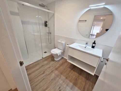 Moderno baño del apartamento BR SILGAR Sanxenxo con ducha walk-in, lavamanos, inodoro y espejo redondo