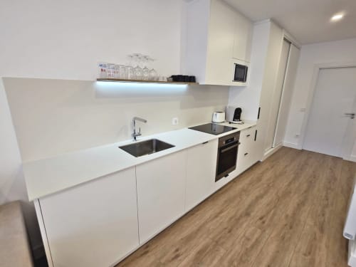 Cocina blanca moderna con fregadero de acero inoxidable, horno negro y suelo de madera en apartamento Silgar, Sanxenxo