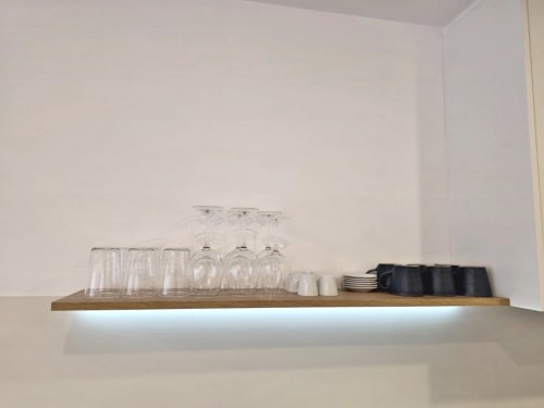 Estante de madera iluminado en apartamento BR SILGAR exhibiendo copas, platos y accesorios de bar en Sanxenxo