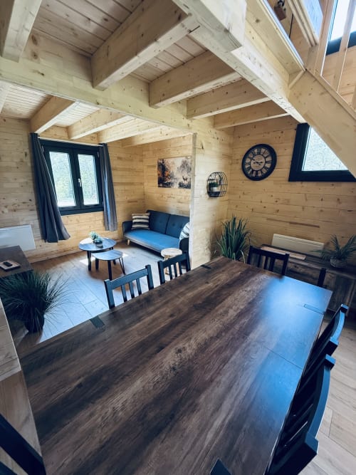 Intérieur de lodge en bois moderne avec table à manger, salon, canapé bleu et plafond aux poutres apparentes aux Cabanes et lodges du