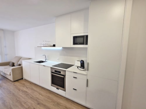 Cocina blanca moderna en apartamento BR SILGAR, Sanxenxo, con electrodomésticos de acero inoxidable y sala de estar abierta