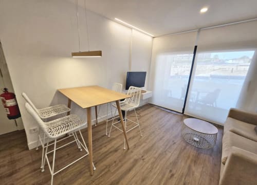 Apartamento moderno en BR Silgar Sanxenxo con mesa de madera, sillas blancas, TV, lámpara colgante y acceso a terraza con vista al mar