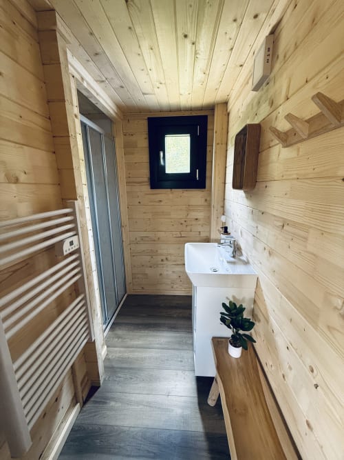 Salle de bain moderne en bois dans un lodge avec lavabo blanc, douche, porte-serviettes chauffant et vue sur les montagnes
