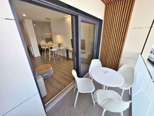 Terraza moderna del apartamento BR Silgar Sanxenxo con sillas blancas, mesa redonda y puertas de cristal que abren al comedor