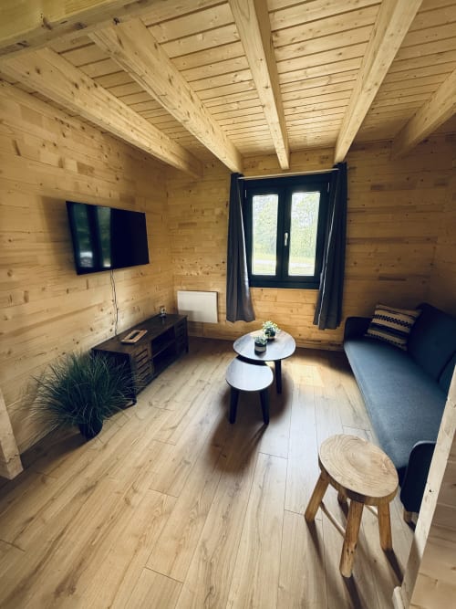 Intérieur de lodge moderne en bois avec téléviseur écran plat, canapé, tables basses rondes et grandes fenêtres donnant sur les montagnes aux Cabanes