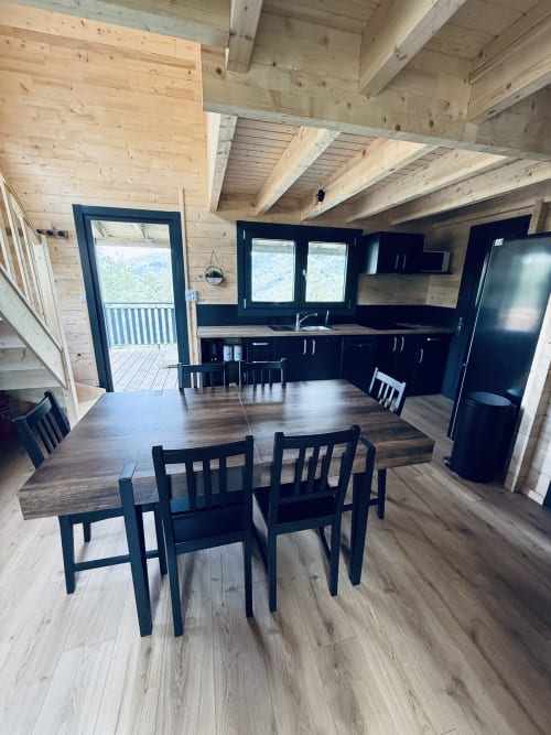 Intérieur de lodge moderne avec cuisine ouverte, salle à manger aux chaises noires, poutres bois et vue montagne