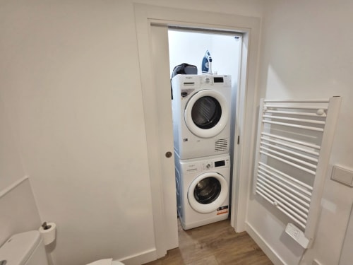 Lavadero con lavadora y secadora apiladas en blanco en el apartamento Sanxenxo Silgar, con toallero y baño visible