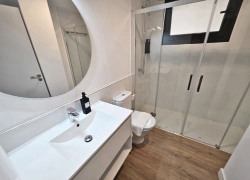 Moderno baño en BR SILGAR Sanxenxo con lavabo blanco, inodoro y cabina de ducha sobre suelo de madera