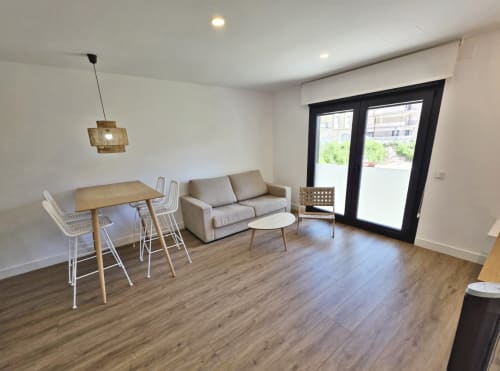 Apartamento moderno en BR Silgar Sanxenxo con sala de estar, mesa de comedor, sofá beige, suelos de madera y puertas de cristal a terraza
