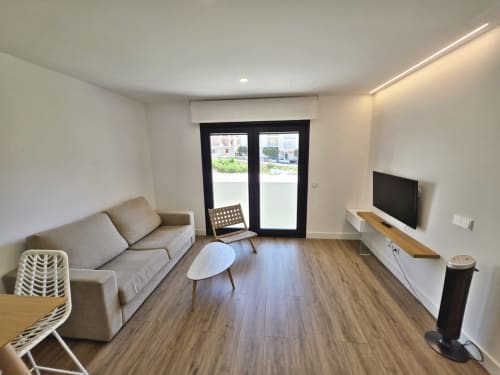 Moderno salón del hotel Silgar de Sanxenxo con sofá, TV, suelos de madera y puertas de cristal a la terraza