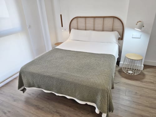 Dormitorio luminoso en BR SILGAR Sanxenxo con cama de cabecero de ratán, ropa de cama blanca, manta en tonos tierra y mesita de mimbre