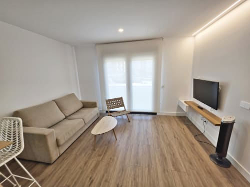 Moderno apartamento en Sanxenxo Silgar con sala de estar, sofá beige, televisor, suelos de madera y acceso a balcón