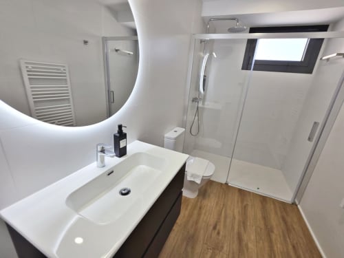 Baño moderno del apartamento BR Silgar Club en Sanxenxo con ducha, espejo iluminado y piso de madera
