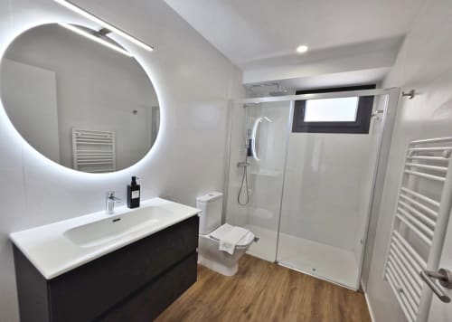 Baño moderno en BR Silgar Club 2 de Sanxenxo con espejo iluminado, mueble de baño negro y mampara de ducha de cristal