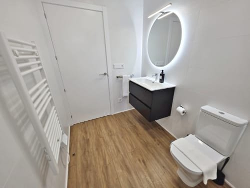 Moderno baño del apartamento BR Silgar Club 2 en Sanxenxo con espejo iluminado, tocador negro, inodoro y suelos de madera