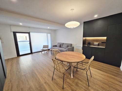 Comedor del apartamento BR Silgar Club 2 con mesa de madera, sillas tejidas, sofá gris, cocina negra e iluminación moderna