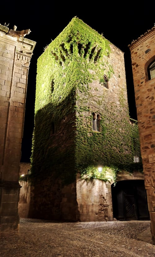 Torre de piedra histórica cubierta de hiedra por la noche, hotel Mirador Medieval en Cáceres, España
