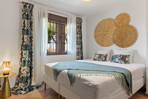 Bright bedroom at Ayma Casa Nísperos in Alhaurín de la Torre with white bed, patterned curtains, and woven wall art.