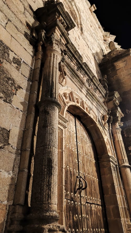Portada medieval de piedra con puerta de madera ornamentada y columna tallada en el hotel Mirador Medieval de Cáceres