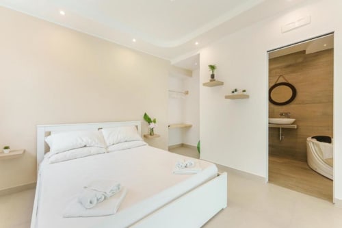 Camera da letto moderna con letto queen al Poeta hotel di Procida: letto bianco, bagno in legno, vasca spa e arredamento minimalista