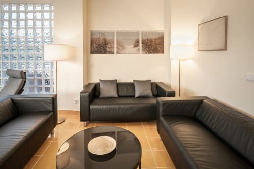 Sala de estar moderna na Villa Odyssey Albufeira com assentos em couro preto, mesa de café em vidro e obra de arte com vista para o mar