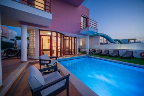 Piscina e pátio iluminados da Villa Odyssey ao entardecer com vista para o mar, Albufeira