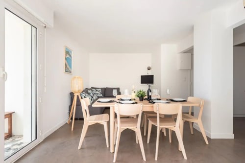 Élégante salle à manger d'appartement moderne avec chaises en bois, table dressée, canapé et accès terrasse vue mer à Saint-Cyr-sur-Mer