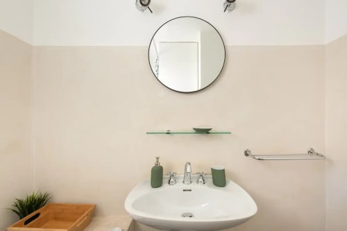Lavabo moderne avec accessoires verts, miroir rond et murs blancs dans un appartement à Saint-Cyr-sur-Mer