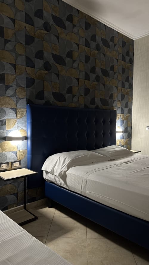 Modern double bedroom at San Paolo Guest House in Rome with blue upholstered bed, geometric patterned wallpaper, and city