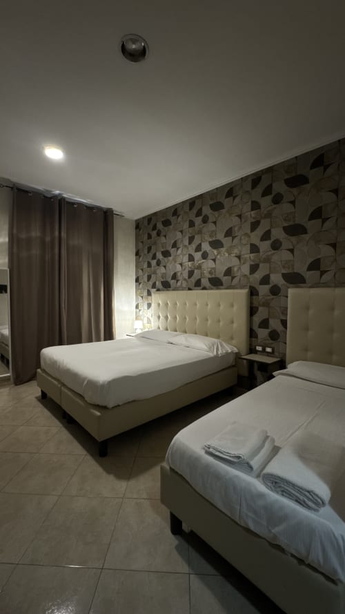 Spacious quadruple bedroom at San Paolo Guest House Rome with twin beds, patterned wallpaper, and modern amenities