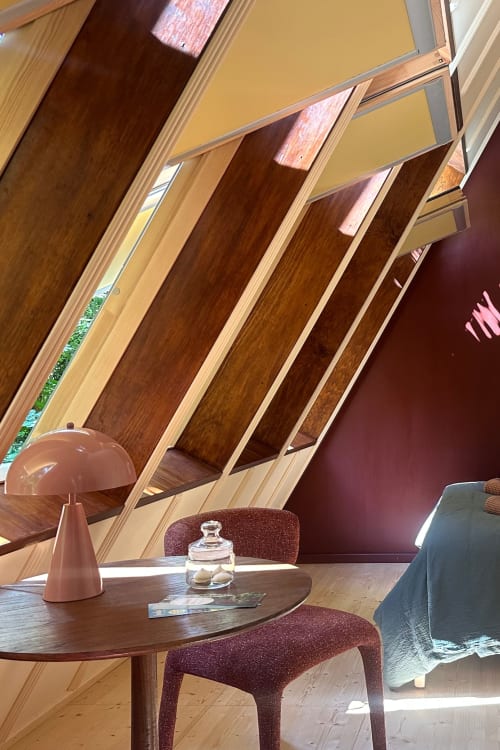 Intérieur bois contemporain aux Micro Palaces BnB de Vaulx avec architecture courbe, table ronde, chaises bordeaux et lampadaire cuivre