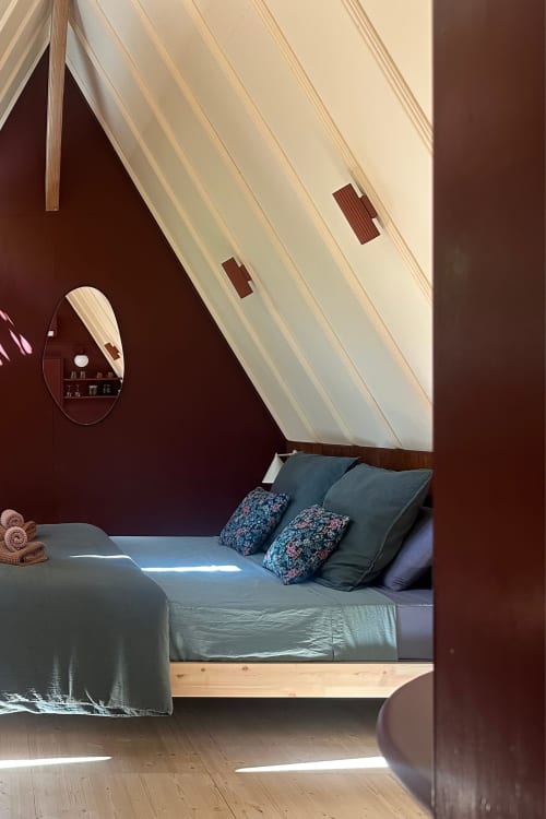 Chambre cosy sous les toits à Micro Palaces Vaulx avec plafond mansardé, literie bleue, miroir rond et murs bordeaux chaleureux
