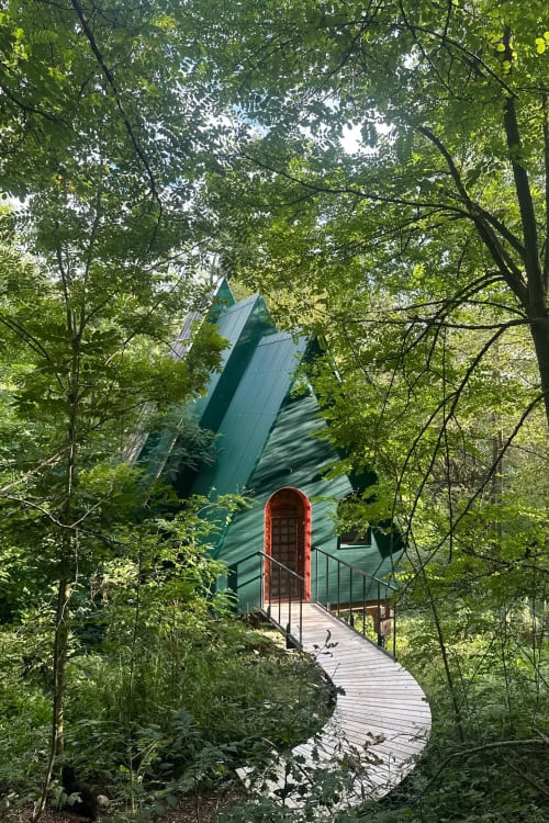 Petite maison en métal vert avec porte rouge nichée dans la canopée forestière aux Micro Palaces, Vaulx FR