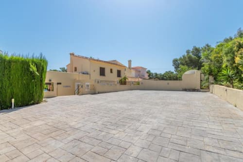 Casa Emilia villa in Moraira with spacious paved driveway, beige Mediterranean architecture, and lush garden views