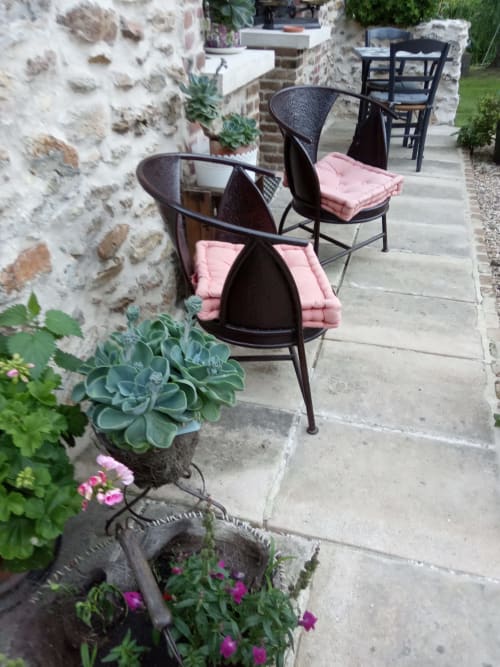 Espace de détente extérieur du Gîte Le Clos du Buisson avec chaises noires, coussins roses, murs en pierre et plantes fleuries à Saint