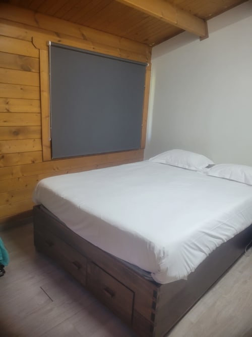 Quarto aconchegante da Casa do Criado Gerês com paredes em madeira, cama queen, roupa de cama branca e TV na parede